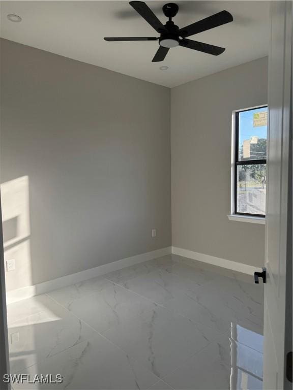 empty room featuring marble finish floor, a ceiling fan, and baseboards