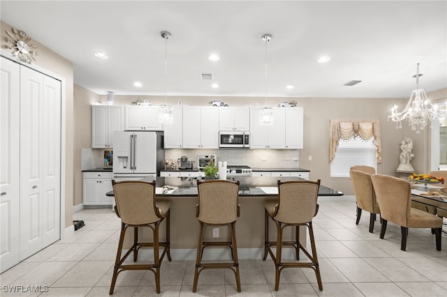 kitchen featuring white cabinetry, high end white fridge, stainless steel microwave, dark countertops, and decorative light fixtures