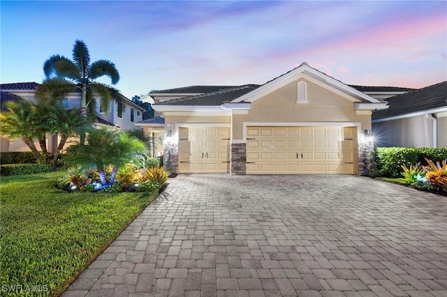 view of front of house featuring stone siding, an attached garage, decorative driveway, a front lawn, and stucco siding