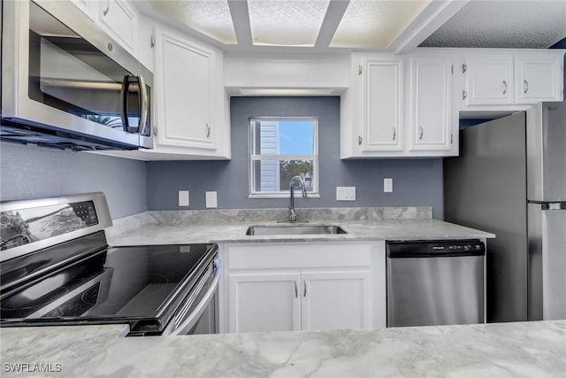 kitchen with white cabinetry, appliances with stainless steel finishes, sink, and light stone counters