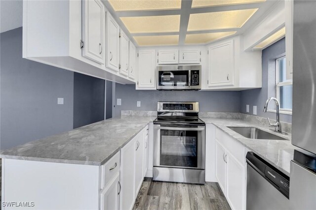 kitchen featuring sink, light hardwood / wood-style flooring, appliances with stainless steel finishes, white cabinets, and kitchen peninsula