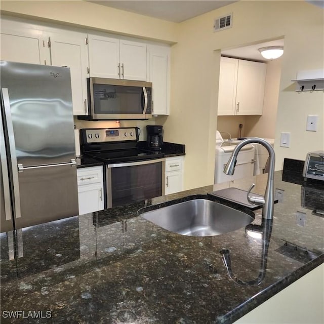 kitchen featuring washer / clothes dryer, dark stone counters, white cabinets, sink, and stainless steel appliances