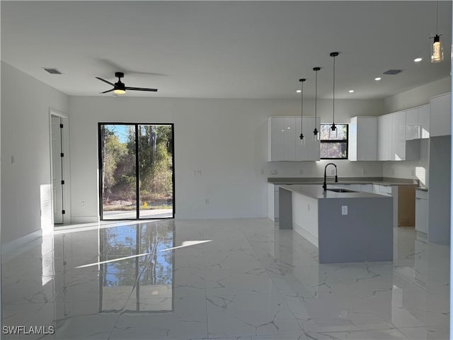 kitchen with an island with sink, sink, pendant lighting, and white cabinets