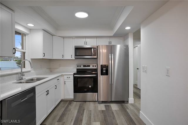 kitchen featuring appliances with stainless steel finishes, sink, light wood-type flooring, white cabinetry, and a tray ceiling