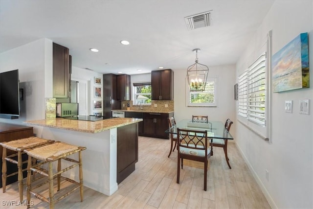 kitchen with light stone countertops, decorative backsplash, dark brown cabinets, pendant lighting, and a breakfast bar