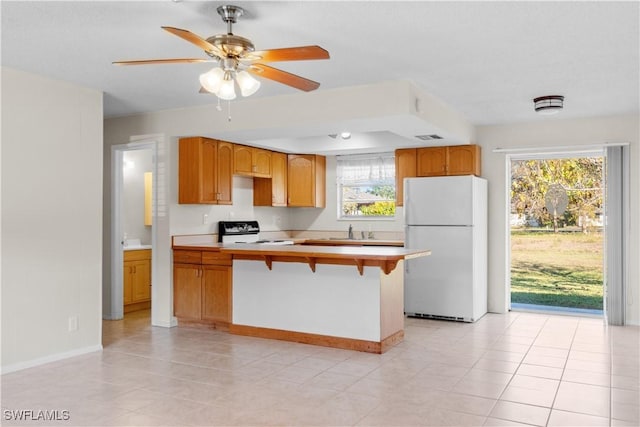 kitchen featuring a kitchen bar, sink, electric range, white fridge, and ceiling fan