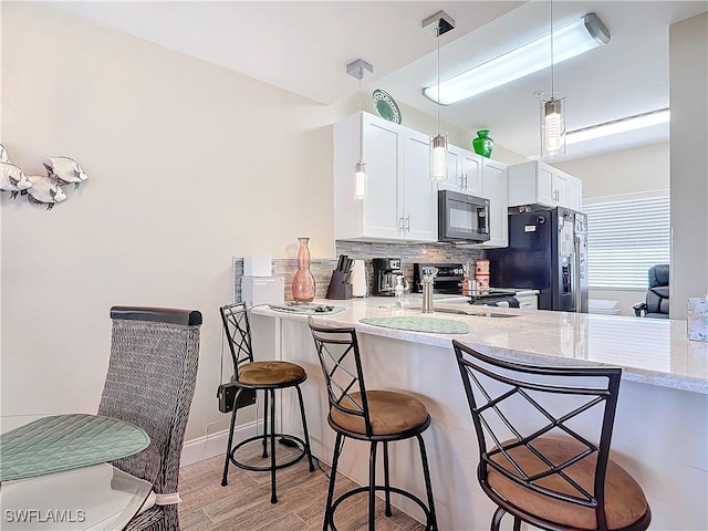 kitchen featuring a breakfast bar, kitchen peninsula, white cabinets, stainless steel fridge with ice dispenser, and electric stove