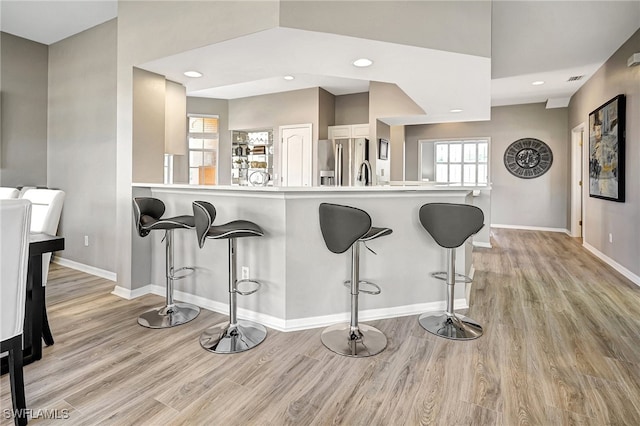 kitchen featuring a breakfast bar, stainless steel fridge, kitchen peninsula, and light hardwood / wood-style floors