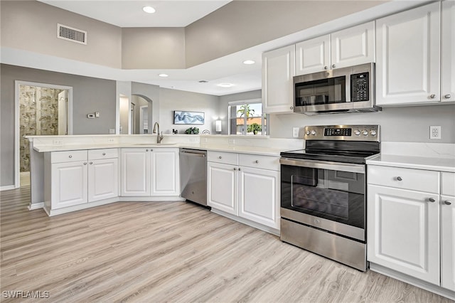 kitchen with sink, white cabinetry, light wood-type flooring, appliances with stainless steel finishes, and kitchen peninsula