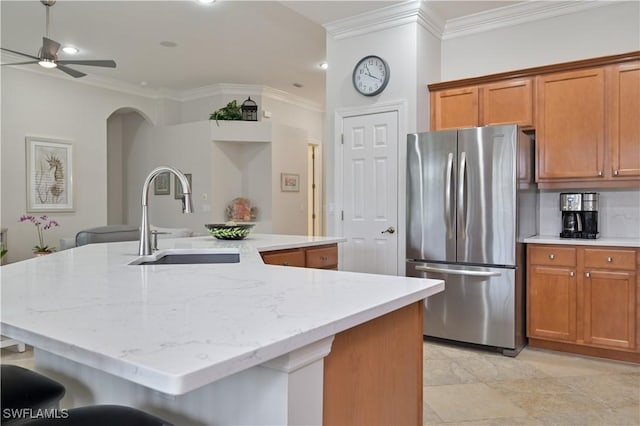 kitchen with sink, crown molding, a kitchen island with sink, and stainless steel refrigerator