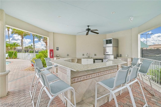 view of patio featuring ceiling fan, a wet bar, and an outdoor kitchen