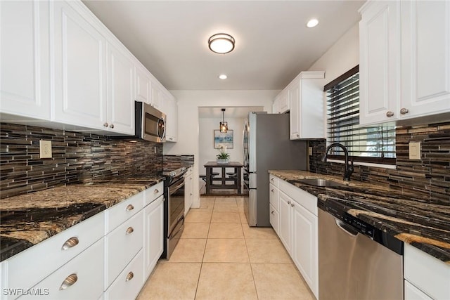 kitchen with sink, dark stone countertops, light tile patterned floors, stainless steel appliances, and white cabinets