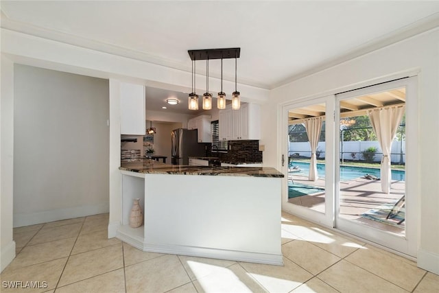 kitchen featuring pendant lighting, white cabinetry, dark stone countertops, stainless steel fridge, and kitchen peninsula