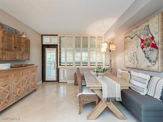 dining room with light tile patterned floors, a textured wall, a textured ceiling, and baseboards