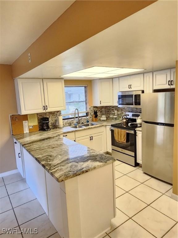 kitchen featuring light stone countertops, appliances with stainless steel finishes, white cabinets, sink, and kitchen peninsula