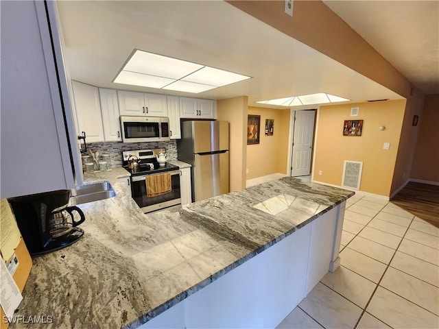 kitchen featuring white cabinets, appliances with stainless steel finishes, tasteful backsplash, kitchen peninsula, and light tile patterned floors