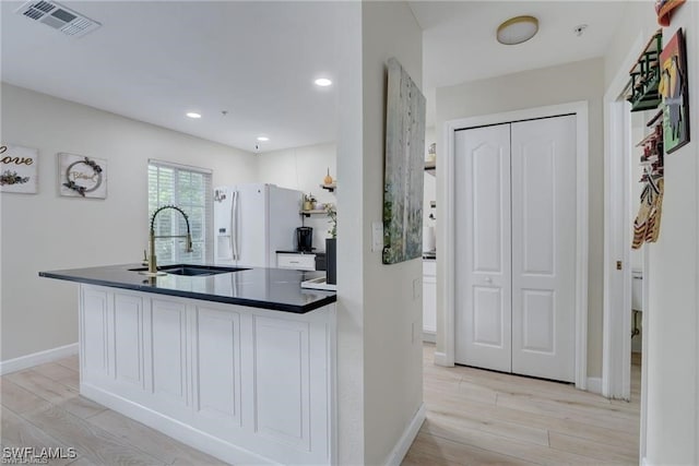 kitchen featuring sink, white fridge with ice dispenser, white cabinetry, and light wood-type flooring