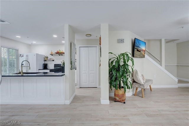 kitchen with sink, light wood-type flooring, black range with electric cooktop, and white fridge