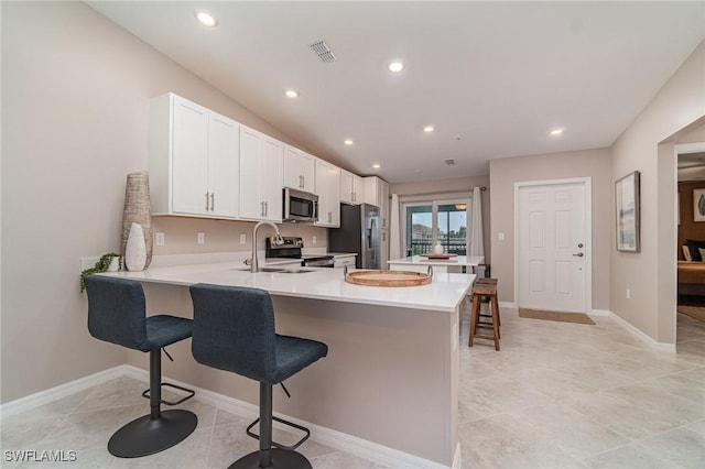 kitchen featuring sink, a kitchen breakfast bar, stainless steel appliances, white cabinets, and kitchen peninsula