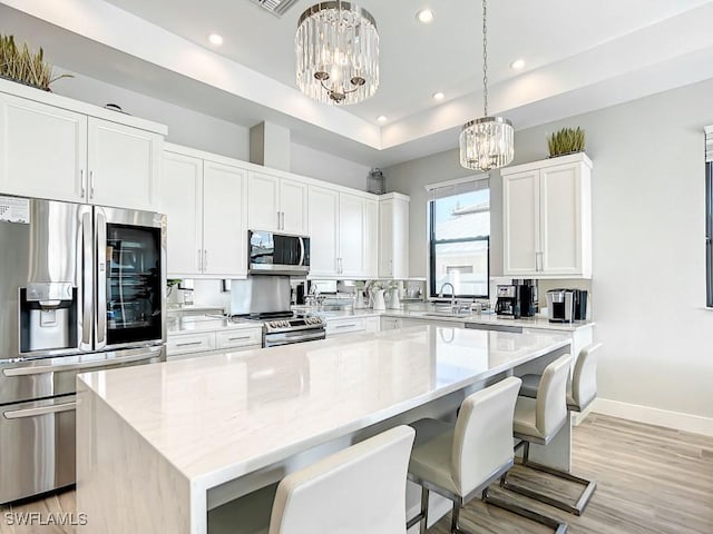 kitchen with white cabinetry, appliances with stainless steel finishes, a center island, and decorative light fixtures