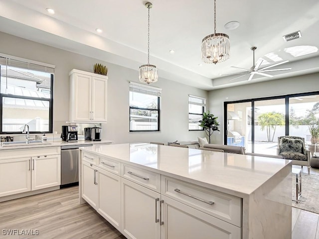 kitchen with decorative light fixtures, white cabinetry, dishwasher, sink, and light stone counters