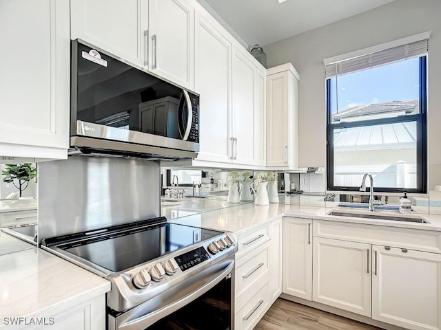 kitchen with sink, light hardwood / wood-style flooring, stainless steel appliances, light stone countertops, and white cabinets