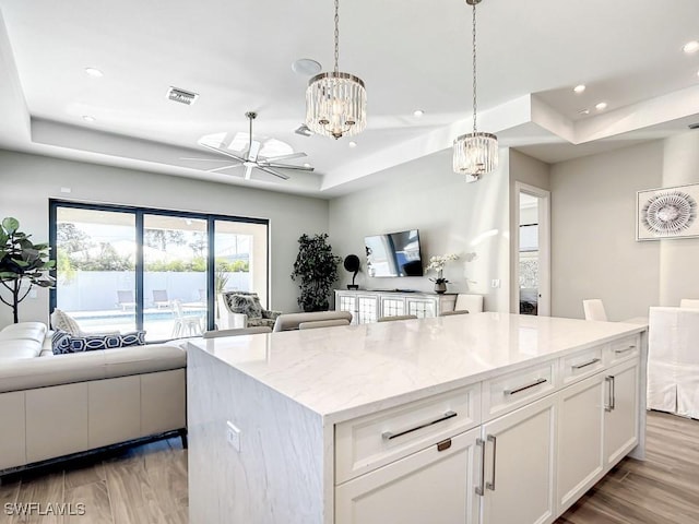 kitchen featuring white cabinetry, a tray ceiling, decorative light fixtures, and a kitchen island