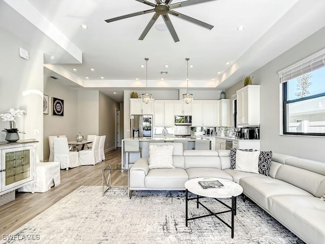 living room featuring ceiling fan, light wood-type flooring, and a tray ceiling