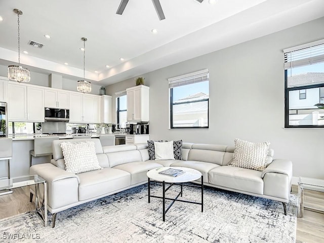 living room featuring a tray ceiling, ceiling fan, and light wood-type flooring