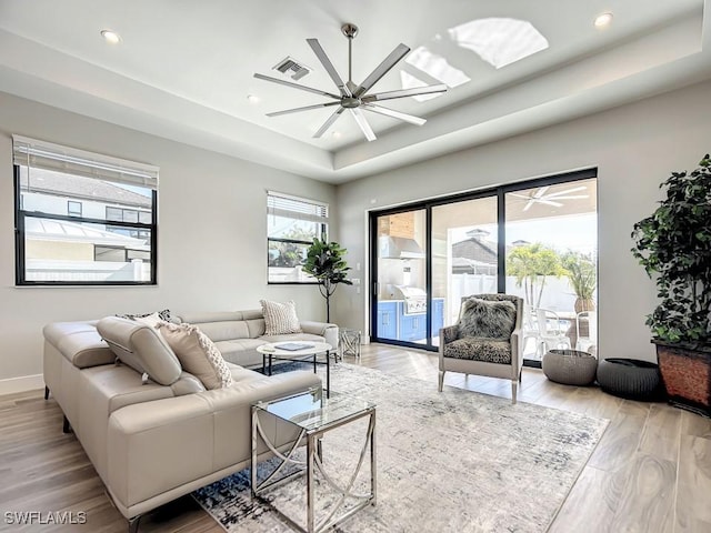 living room with a tray ceiling, light hardwood / wood-style flooring, and ceiling fan