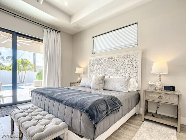 bedroom with access to exterior, light hardwood / wood-style floors, and a tray ceiling