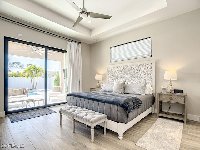 bedroom featuring access to exterior, a raised ceiling, ceiling fan, and light wood-type flooring