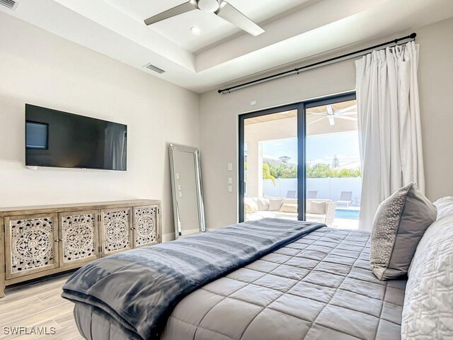 bedroom featuring ceiling fan, access to exterior, light wood-type flooring, and a tray ceiling