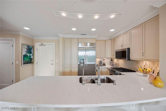 kitchen with sink, appliances with stainless steel finishes, ornamental molding, kitchen peninsula, and cream cabinetry