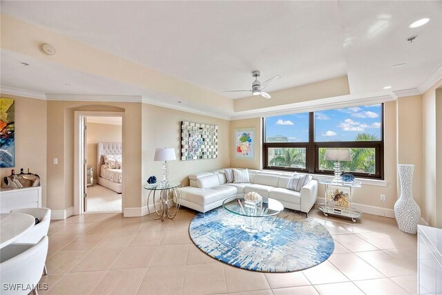 tiled living room with ornamental molding, ceiling fan, and a tray ceiling