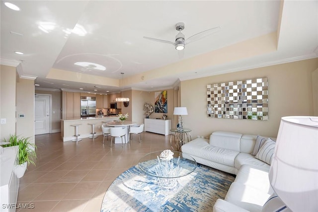 living room featuring light tile patterned flooring, ceiling fan, a tray ceiling, and ornamental molding