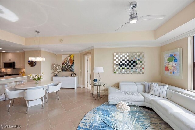 tiled living room featuring a raised ceiling, crown molding, and ceiling fan with notable chandelier