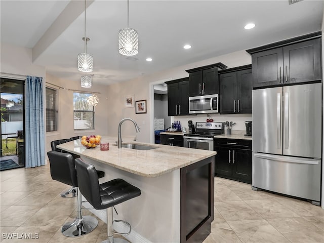 kitchen with sink, decorative light fixtures, light stone countertops, an island with sink, and stainless steel appliances