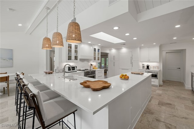 kitchen with kitchen peninsula, pendant lighting, sink, white cabinets, and a kitchen bar