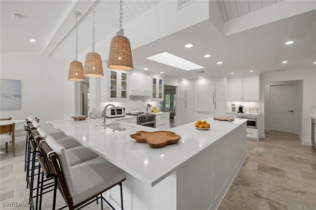 kitchen featuring white cabinets, stone tile floors, a breakfast bar, a sink, and a skylight