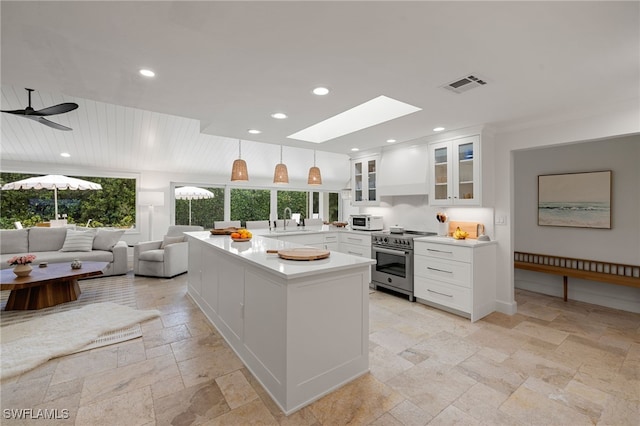 kitchen with stone tile floors, visible vents, high end range, premium range hood, and a sink