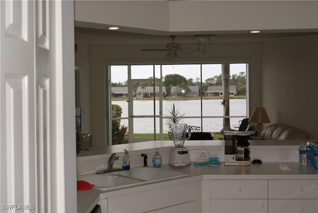 kitchen with white cabinetry, a water view, ceiling fan, and sink