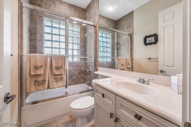 full bathroom featuring combined bath / shower with glass door, vanity, and toilet