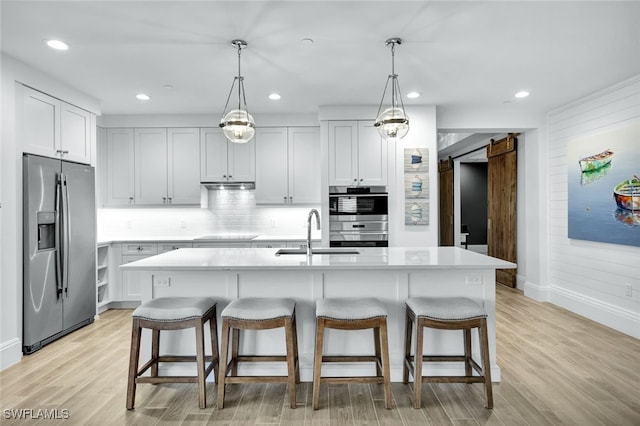 kitchen featuring a barn door, an island with sink, appliances with stainless steel finishes, and sink