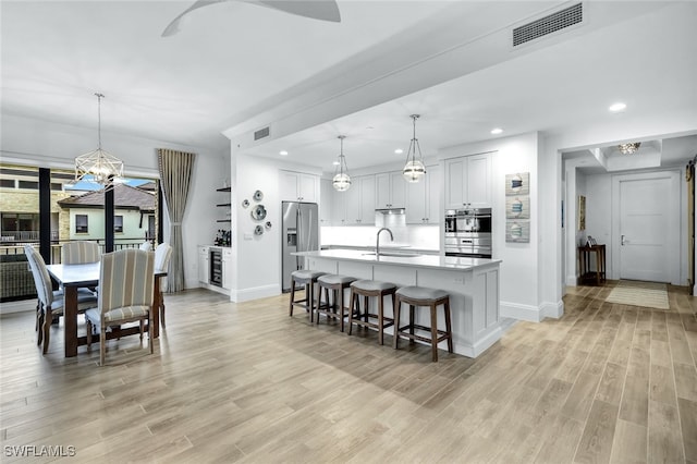 kitchen with a center island with sink, stainless steel fridge, hanging light fixtures, and white cabinets