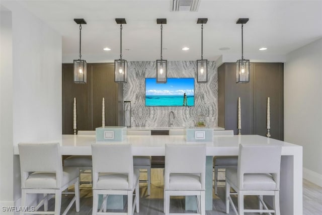 bar featuring hanging light fixtures, dark brown cabinets, and light wood-type flooring