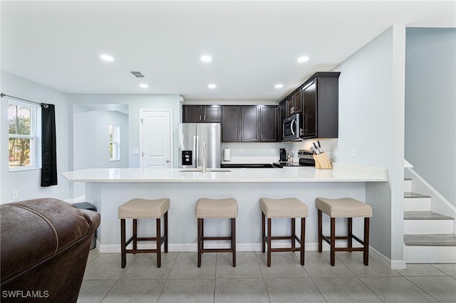 kitchen featuring dark brown cabinetry, stainless steel appliances, kitchen peninsula, and a kitchen bar