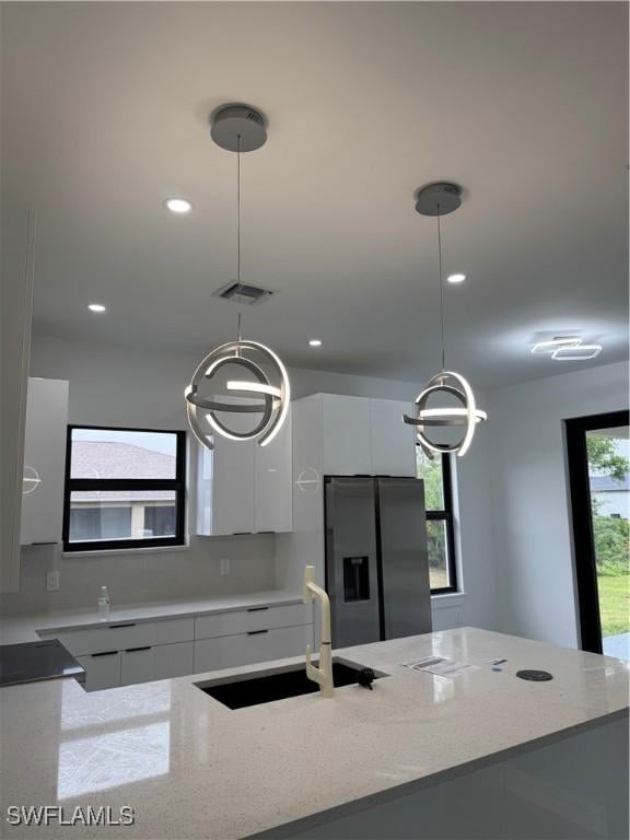 kitchen with pendant lighting, sink, white cabinetry, light stone counters, and stainless steel fridge with ice dispenser