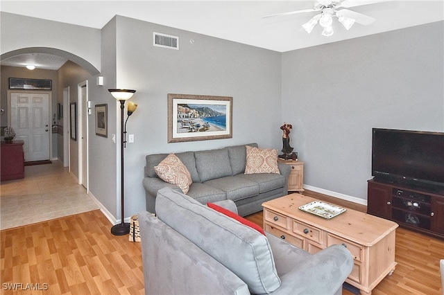 living room featuring arched walkways, light wood finished floors, visible vents, and baseboards