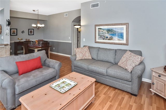 living room with baseboards, visible vents, arched walkways, light wood-style flooring, and a chandelier